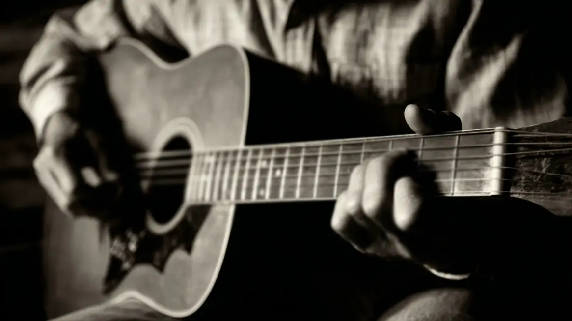 Close-up black-and-white photo of a person playing an acoustic guitar, focusing on their hands and the guitar strings