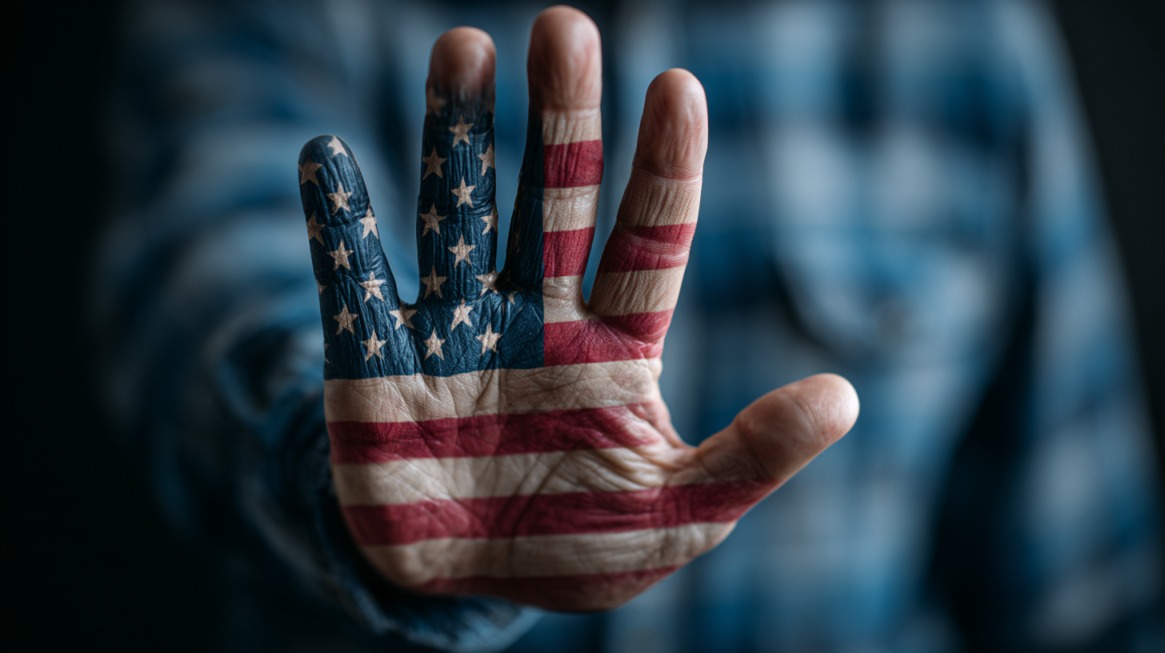 Close-up of a hand with the U.S. flag painted across it, held up in a stop gesture, symbolizing denial or refusal