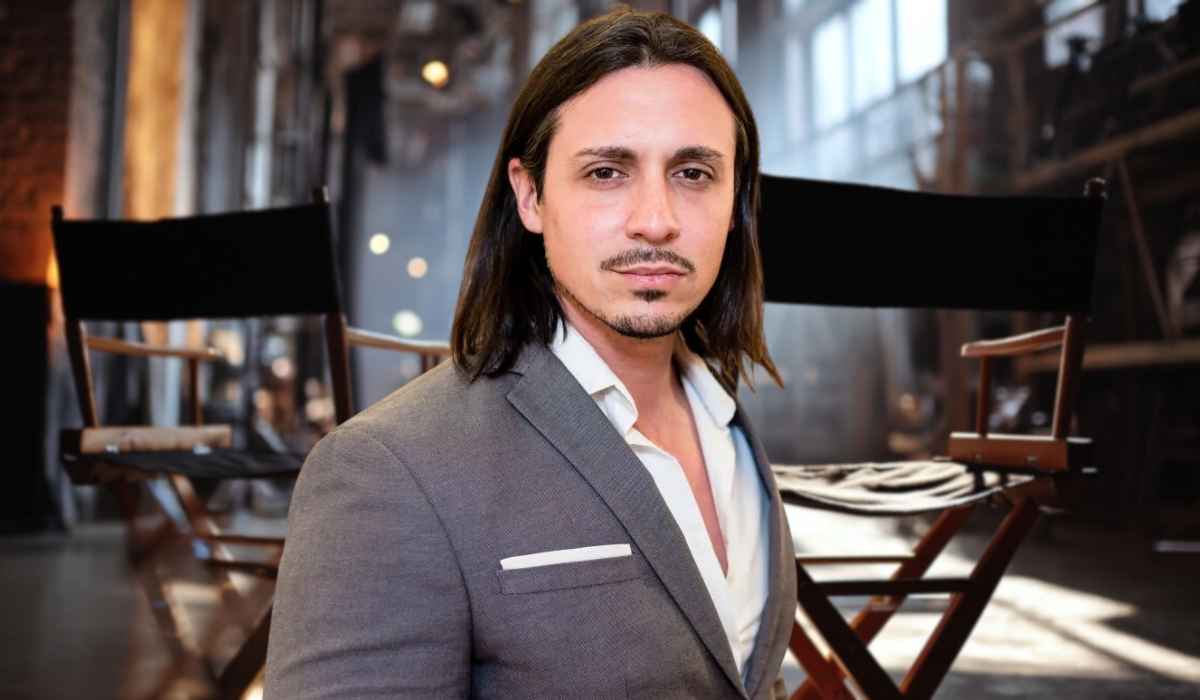 Peter Madrigal in a suit standing in front of director’s chairs on a film set