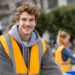 Young volunteer wearing an orange safety vest smiling while helping at an outdoor community event