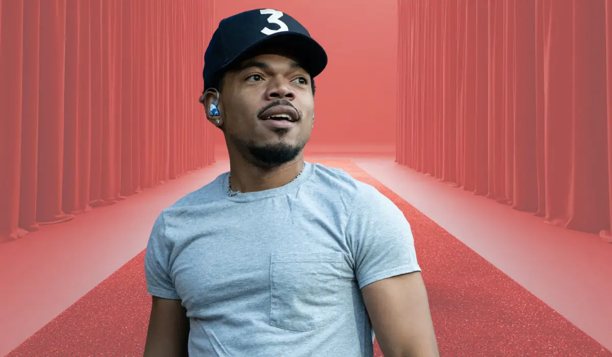 Person wearing a cap and T-shirt standing on a red carpet with curtains in the background