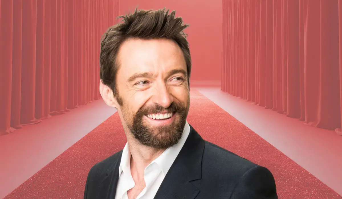 A man smiling while standing on a red carpet with curtains in the background