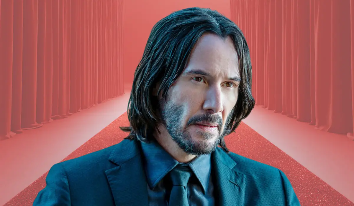 Person in a suit standing on a red carpet with curtains behind