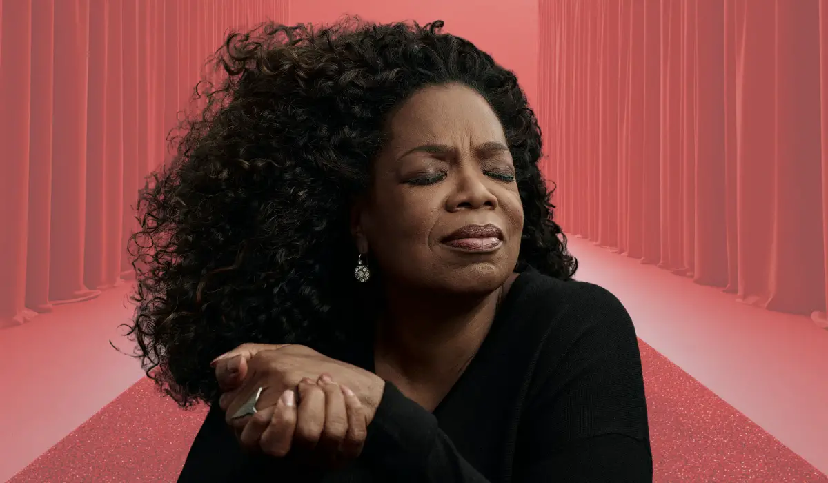 Portrait of a woman with curly hair and closed eyes, holding her hands together against a soft red background