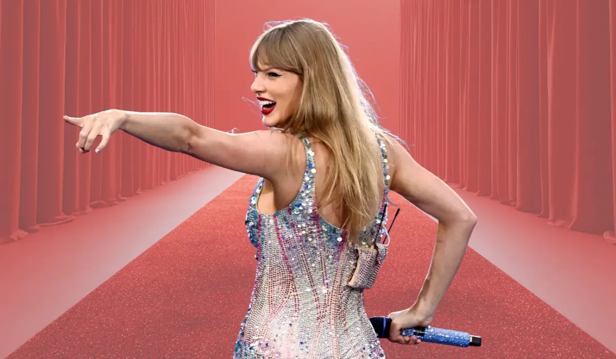 Smiling performer pointing outward while holding a microphone on a red carpet–style background