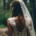 Back view of a bride in a lace wedding dress standing on a forest path