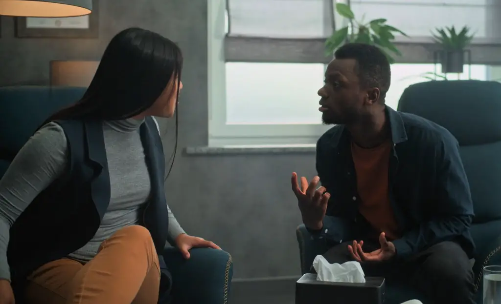 Two people talk intensely in an office setting, expressing concern and frustration