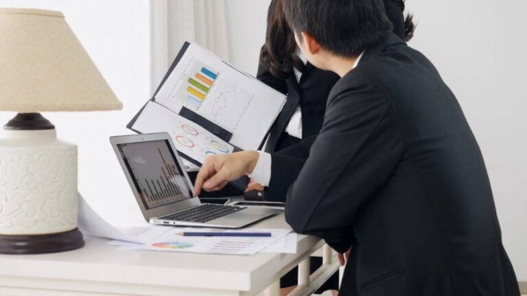 A team reviews charts on a laptop and documents during a meeting about how to start a business