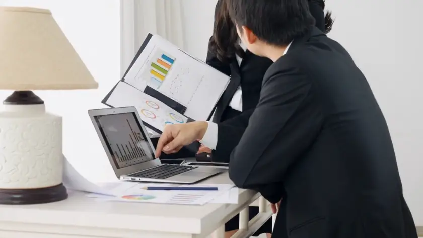 A team reviews charts on a laptop and documents during a meeting about how to start a business