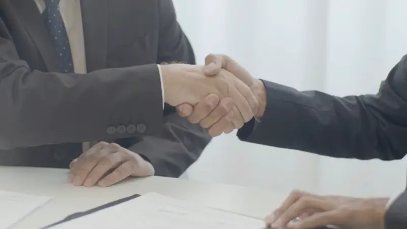 Two professionals shake hands over signed client documents