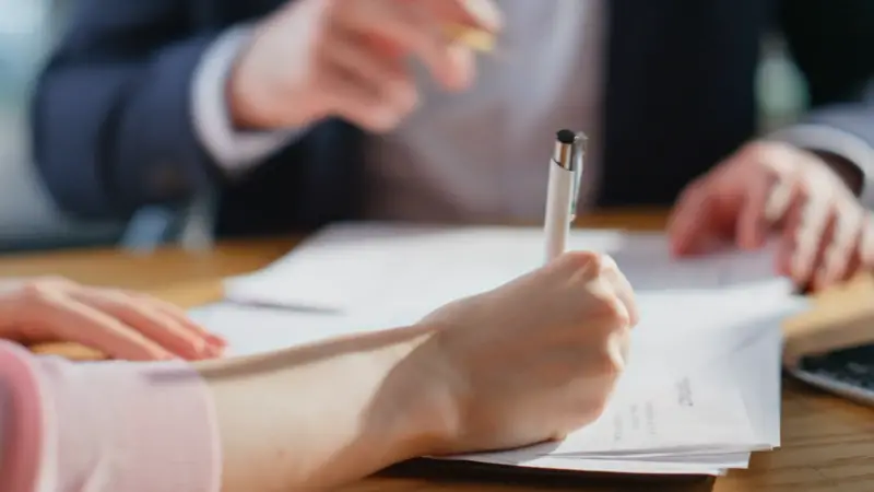 A person signs documents during a discussion about company policies