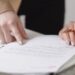 Hands review and sign paperwork on a desk for legal protection