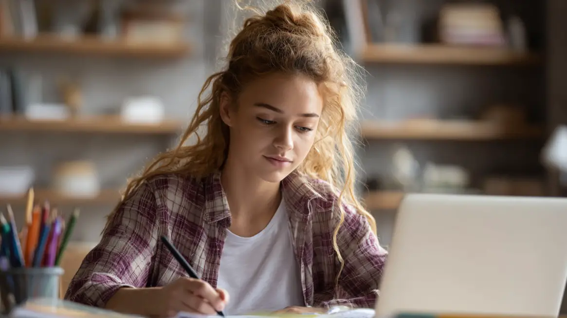 Young woman studying at a desk with a laptop and notebook in a cozy workspace