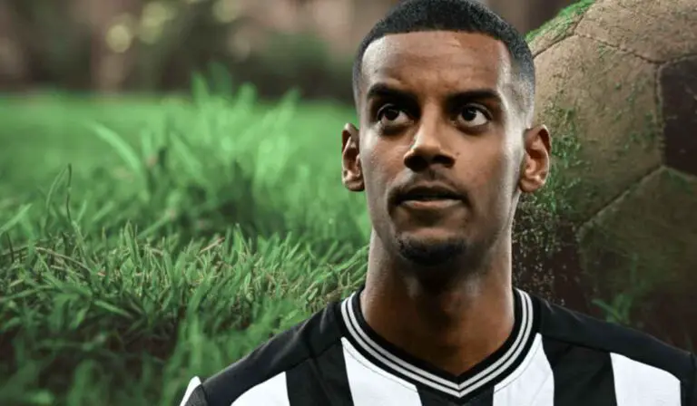 Close up of a football player in a black and white jersey standing in front of a grassy background with a soccer ball behind him