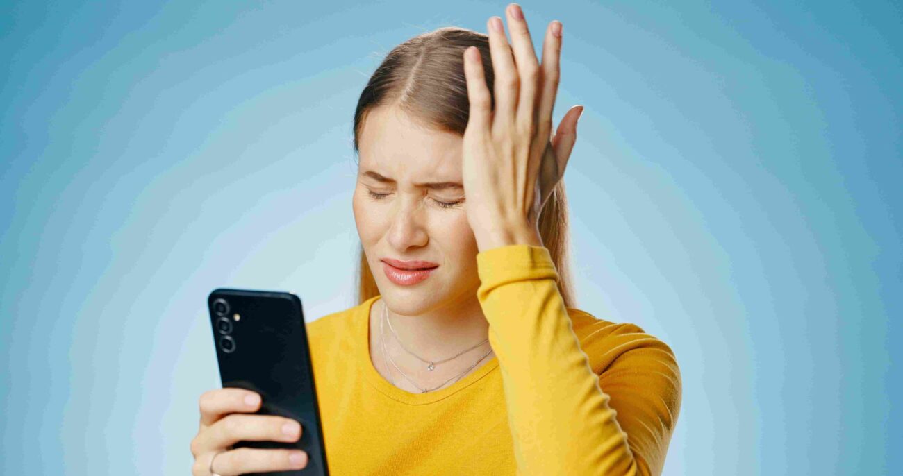 Frustrated woman holding a smartphone and touching her forehead while looking at the screen