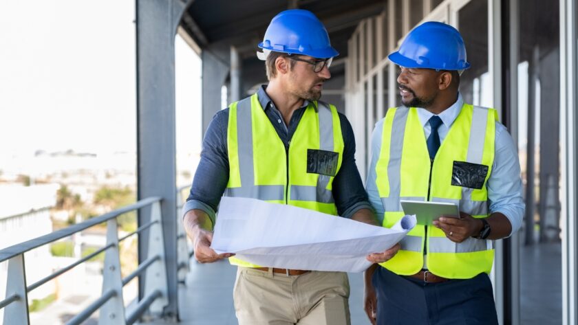 Two construction managers review plans inside an unfinished building