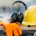 Yellow hard hat, gloves, safety glasses, and ear protection sit on a construction site table