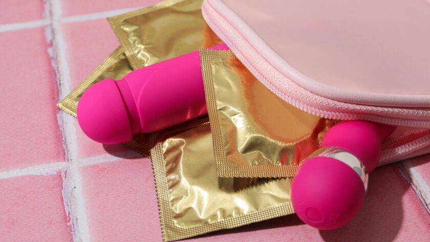 Pink intimate wellness products placed beside gold condom wrappers