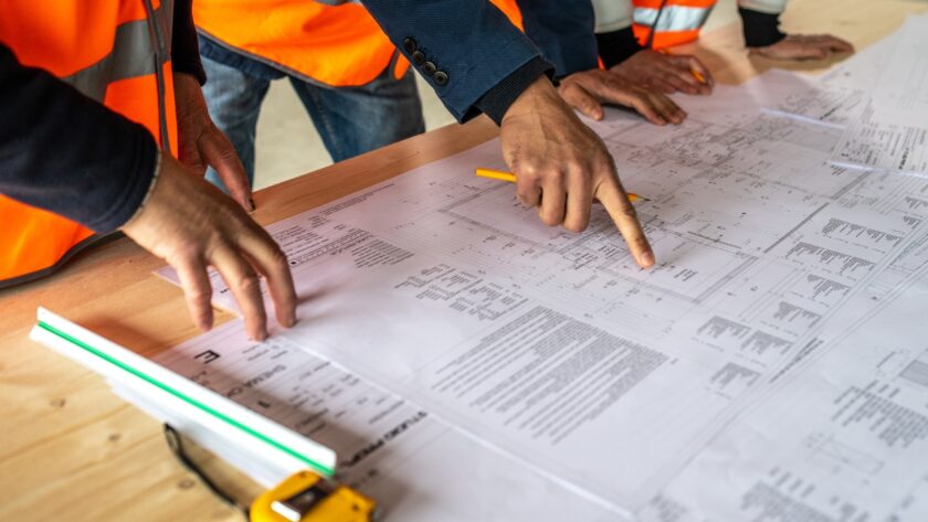 Construction workers review project plans across a large blueprint on site