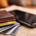 Close-up of a smartphone next to a leather wallet containing multiple payment cards, representing digital and traditional payment methods
