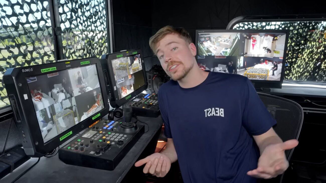 Man speaking inside a production control room surrounded by video monitors and broadcast equipment.