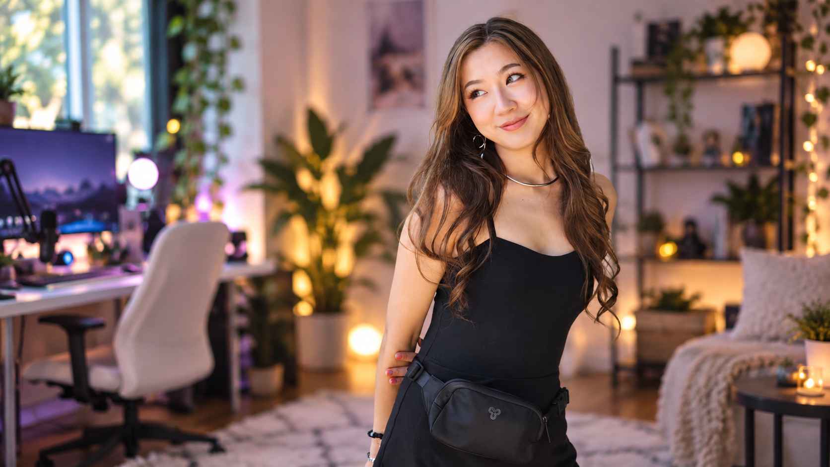 Fuslie standing in a cozy gaming room with a streaming setup in the background.