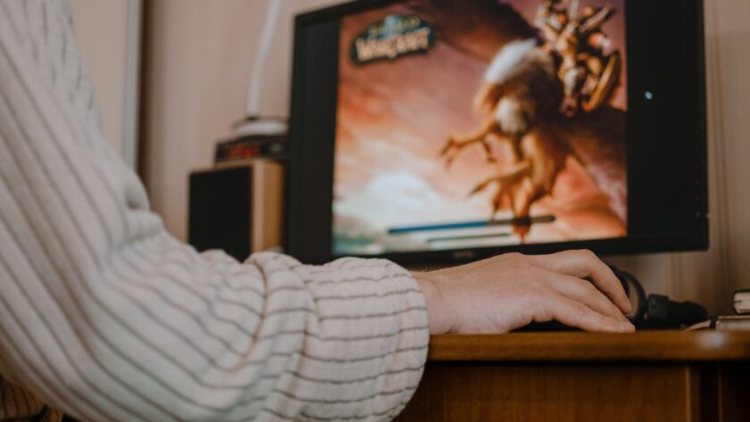A person uses a computer with World of Warcraft visible on the screen