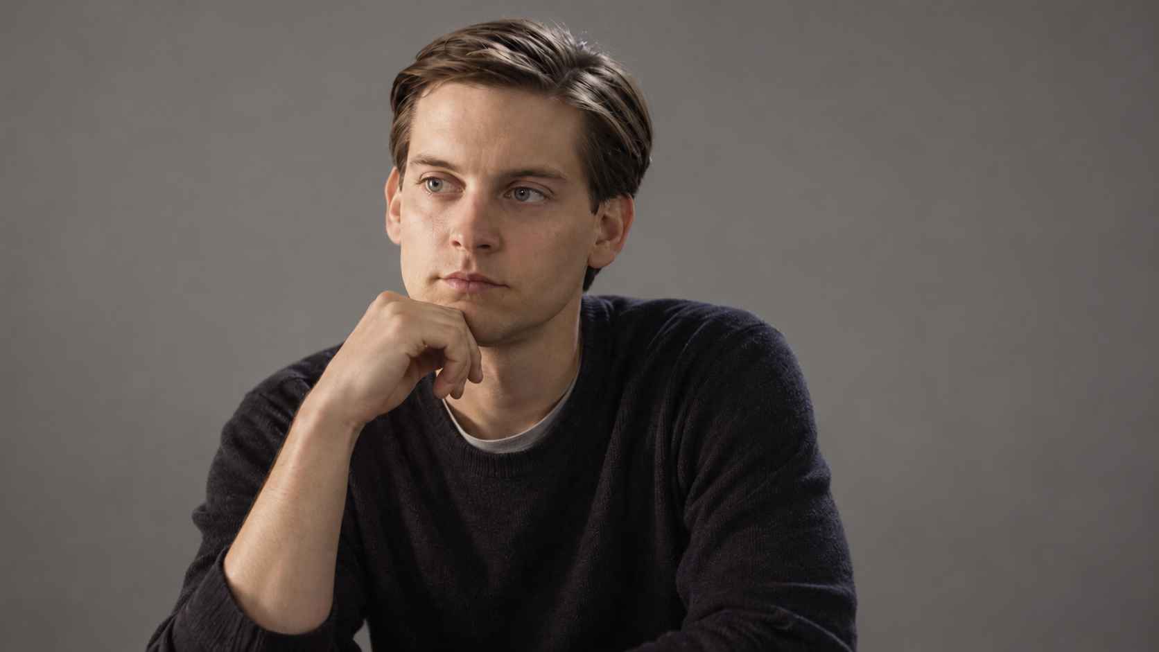 Young Tobey Maguire in a dark sweater against a plain grey background.
