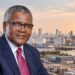 Aliko Dangote pictured against an industrial backdrop featuring an oil refinery, cement facilities, and cargo ships.